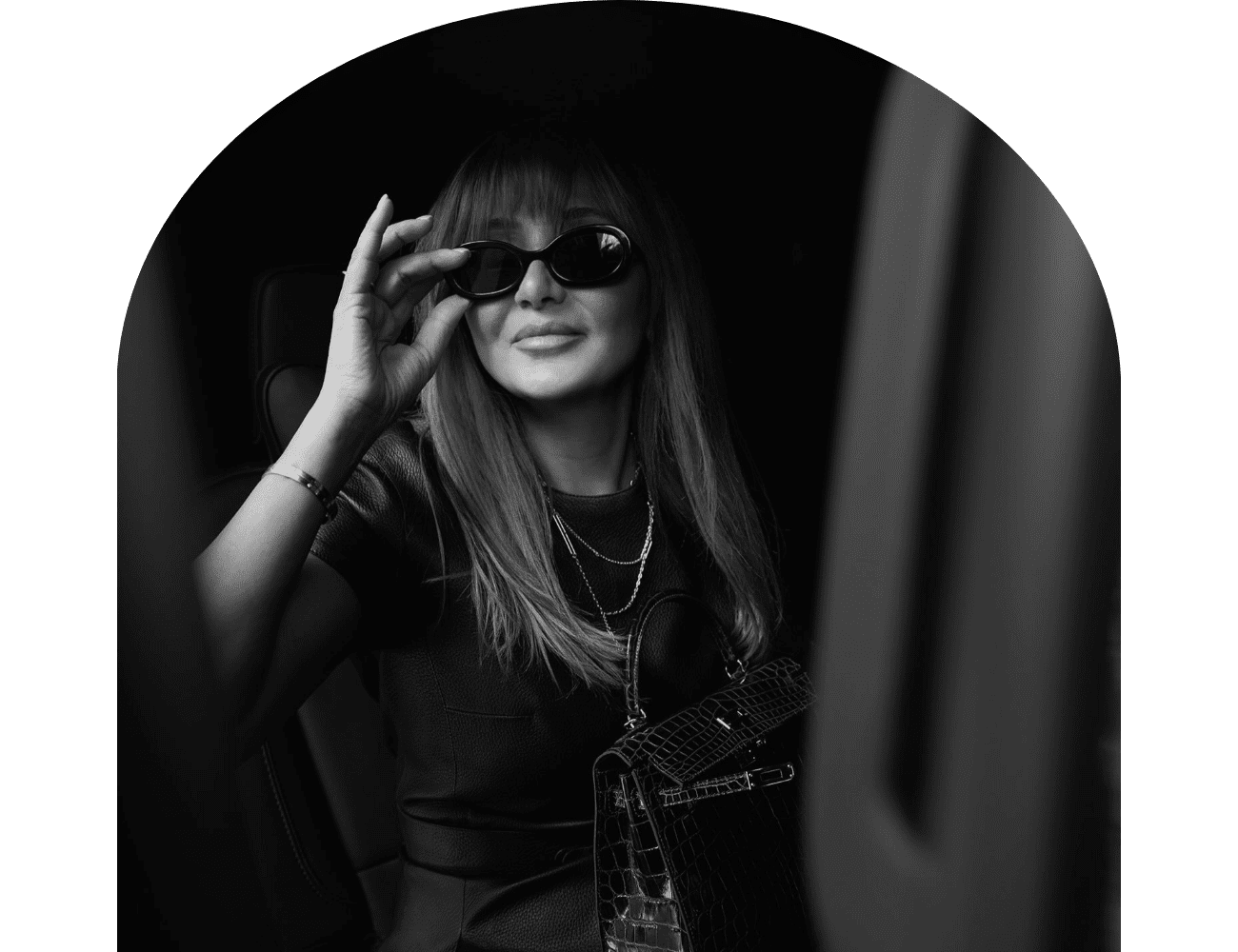 Stylish woman in sunglasses, seated in a car, holding a textured handbag.