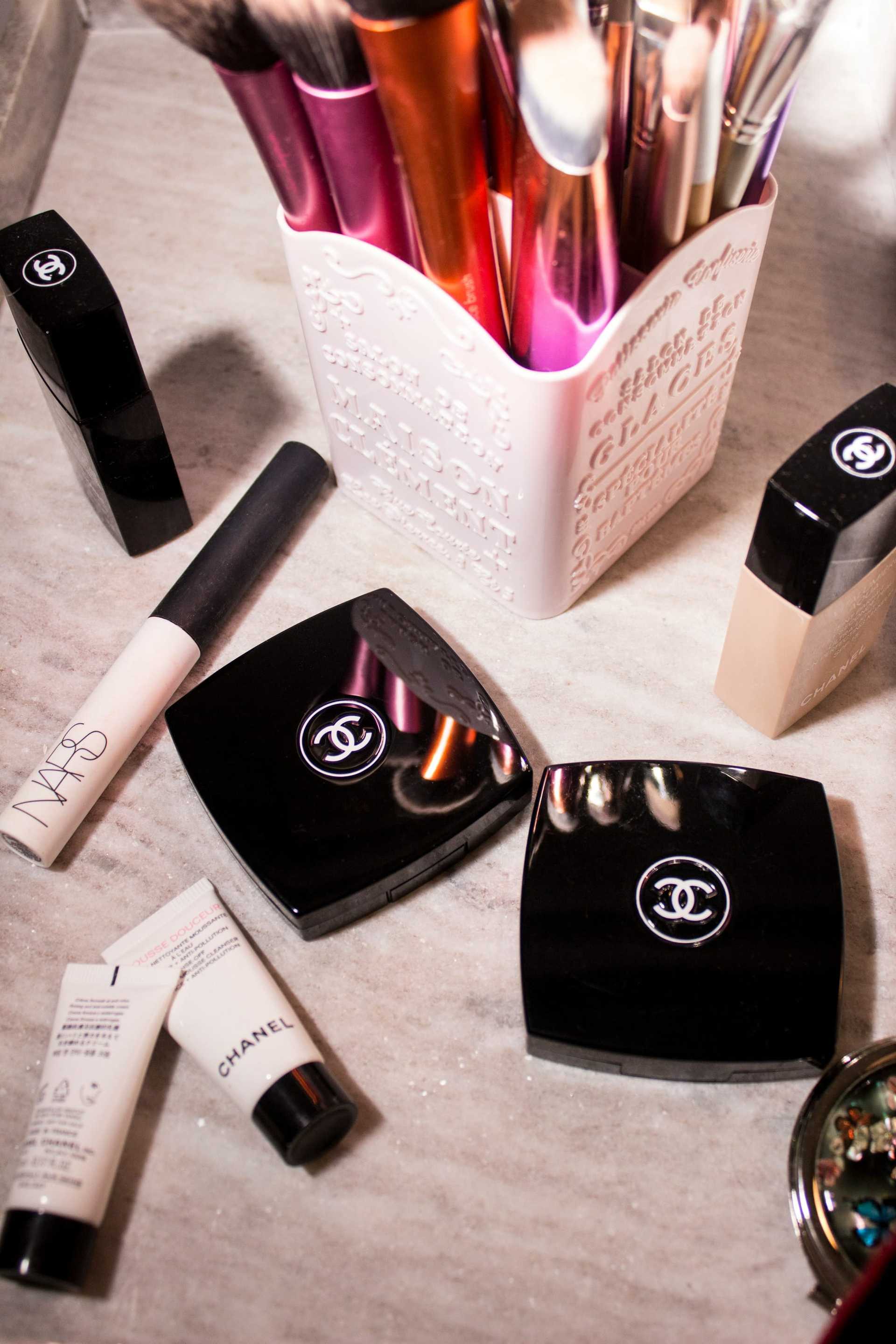 Makeup products arranged on a marble surface, including brushes, compacts, and foundation.