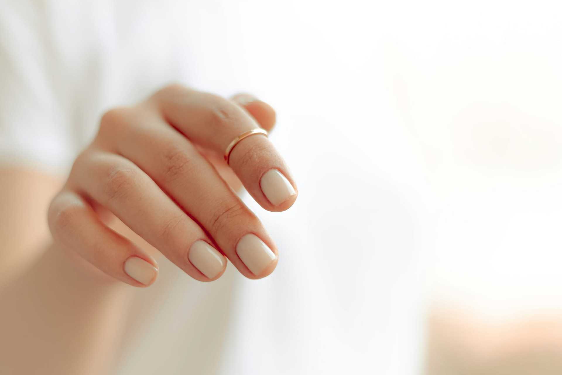 Close-up of a hand with a gold ring on the finger and neutral-colored nail polish.